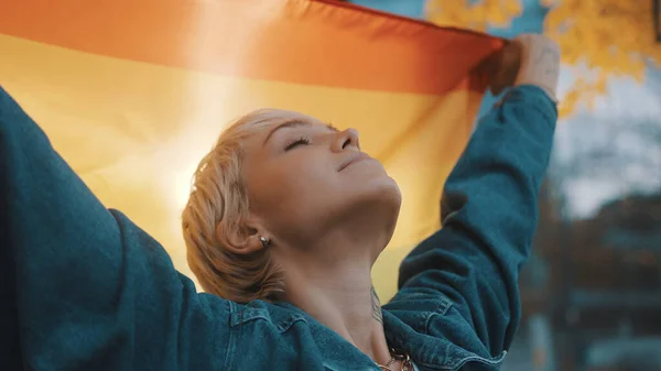 Hermosa mujer joven con el pelo corto ondeando la bandera del arco iris en el parque — Foto de Stock