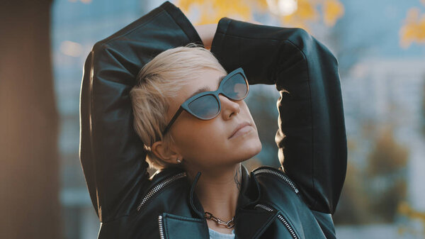 Close up portrait of joyful young woman with bright hair and sunglasses standing with hands over the head. People and style concept.