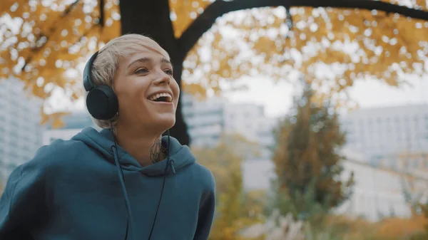 Porträtt av ung blond kvinna som lyssnar på musik i parken med hörlurar på höstdagen — Stockfoto