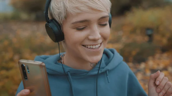 Die junge blonde Frau hört im Park über Kopfhörer Musik von ihrem Smartphone. Porträt — Stockfoto