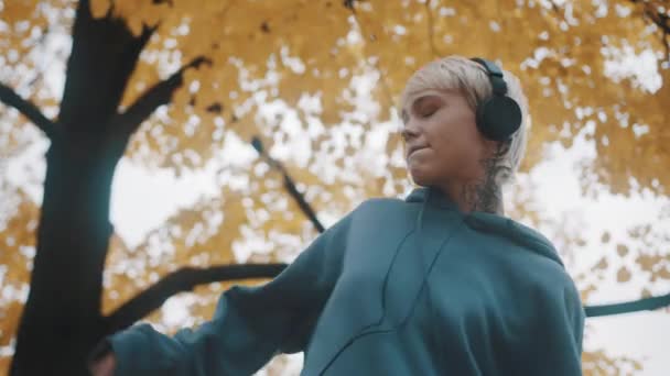 Crazy young woman dancing in the park in autumn with headphones. Low angle — Stock Video