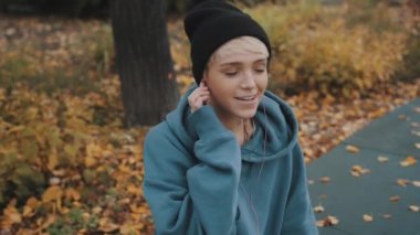 Siyah şapkalı deli, kendine güvenen genç bir kadın parkta kulaklık takarak akıllı telefondan müzik dinliyor.