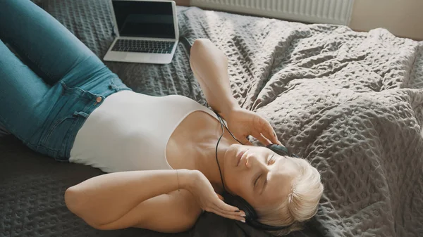 Молодая счастливая женщина слушает музыку в наушниках в своей спальне — стоковое фото