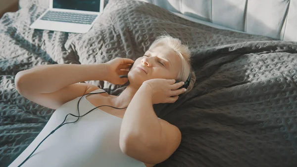 Joven mujer feliz escuchando la música en los auriculares en su dormitorio — Foto de Stock