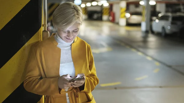 Молодая модная блондинка-кавказка пользуется смартфоном в подземном гараже — стоковое фото