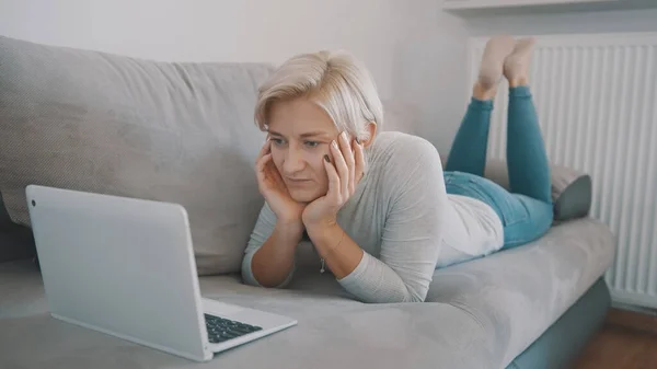 Joven mujer dura charlando con amigos en las redes sociales utilizando el ordenador portátil en su sofá. — Foto de Stock