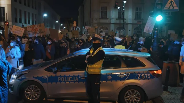 Varsovia, Polonia 30.10.2020 - Protesta contra el aborto y los derechos humanos, huelga de mujeres, manifestantes que pasan cerca de un coche de policía iluminado por la luz de emergencia —  Fotos de Stock