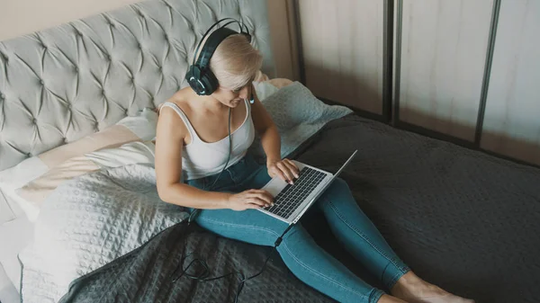 Mujer joven usando portátil en su dormitorio. Freelancer trabajando desde la comodidad de su hogar — Foto de Stock