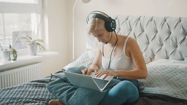 Молодая женщина использует ноутбук в своей спальне. Фрилансер, работающая не выходя из дома — стоковое фото