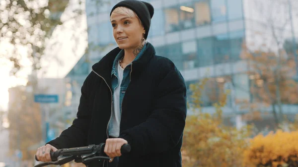 Jonge vrouw in winter zwarte jas met hoed paardrijden electische scooter in het stadspark. Ecologisch openbaar vervoer. Concept van eco-leven, actieve levensstijl — Stockfoto