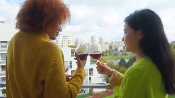 Mujeres jóvenes multirraciales de pie juntas en el balcón y bebiendo vino tinto. Pareja lesbiana disfrutando de vacaciones — Vídeos de Stock