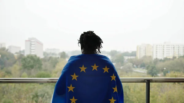 Jeune homme afro-américain couvert du drapeau de l'UE debout sur le balcon — Photo