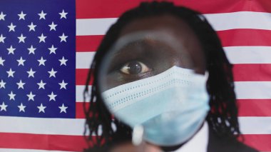 Maskeli Afro-Amerikan Adam, Amerika Birleşik Devletleri bayraklı arka planına yakın bir büyüteç tutuyor - Büyütülmüş Göz - Yakın çekim