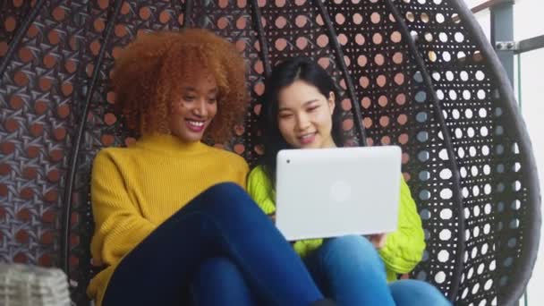 Dos mujeres relajándose en el columpio, y navegando por las redes sociales. Africano americano y asiático mujer, multirracial amistad concepto — Vídeos de Stock