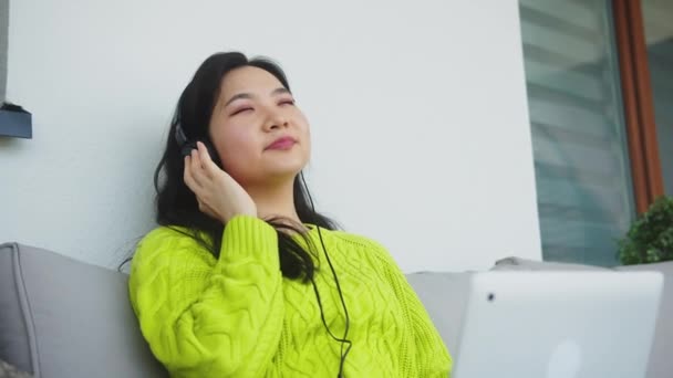 Mladá asijská žena poslech hudby z notebooku pomocí sluchátek — Stock video
