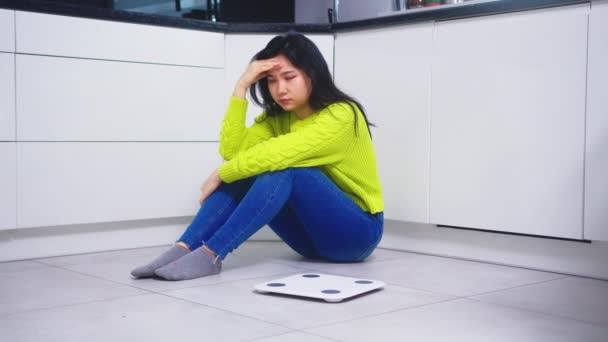 Frustré suivre un régime jeune femme asiatique assis sur le flor avec la balance de poids devant. Concept de perte de poids et de santé mentale — Video