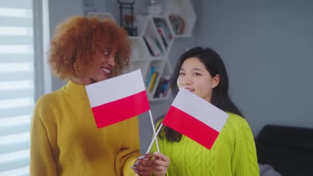 Amistad e igualdad multirraciales. Mujer afroamericana y asiática sosteniendo bandera polaca. Programa de intercambio de estudiantes — Vídeo de stock