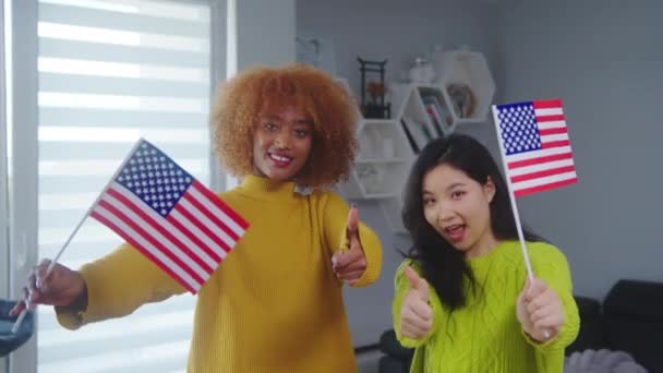 Flerkulturelt vennskap og studentutveksling. Afrikansk-amerikansk og asiatisk kvinne med USA-flagg med tommeltotter opp – stockvideo