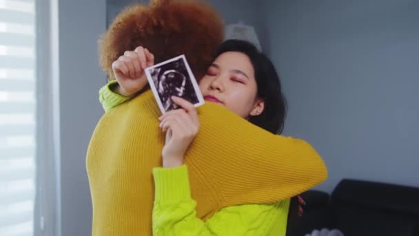 Pareja lesbiana multirracial esperando un bebé. Abrazando con ultrasonido imagen del bebé. Apoyo a la maternidad — Vídeos de Stock