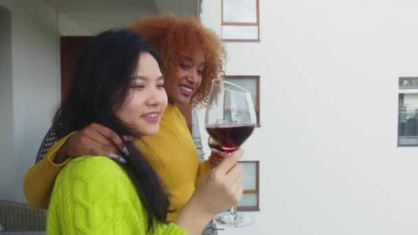 Διαφυλετικό ζευγάρι φιλενάδων που πίνουν κρασί στο μπαλκόνι . — Αρχείο Βίντεο