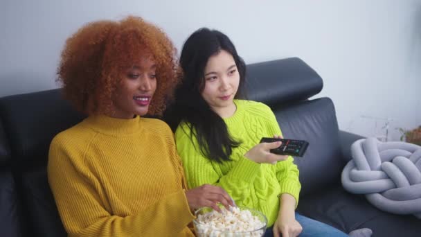 Многорасовая дружба. Afican America black and asian woman eating popcorns and watching movies — стоковое видео