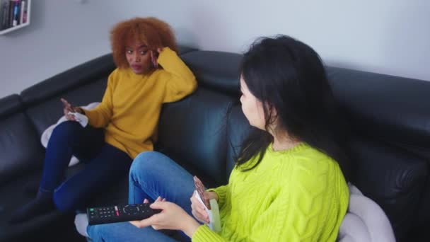 Twee vrouwen in de woonkamer kijken televisie roddelend en pralines etend — Stockvideo