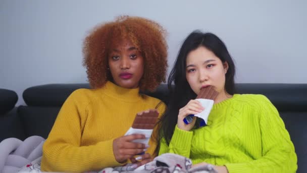 Nudí se, studenti sedí na gauči přikrytí přikrývkou a koukají na televizi a jedí čokoládu — Stock video
