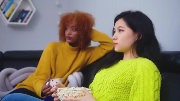 Çok ırklı dostluk. Afro-Amerikan siyah ve Asyalı kadın patlamış mısır yiyor, dedikodu yapıyor ve film seyrediyor. Flört ediyorlar ve birbirlerine bakıyorlar. — Stok video