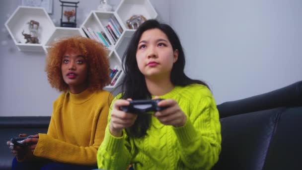 Alegre feliz meninas atraentes jogando videogames em casa. Focado asiático mulher perder o jogo de Africano americano preto amigo — Vídeo de Stock