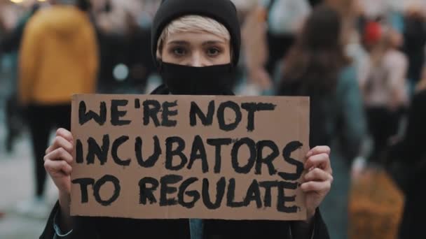 Marsz kobiet. Młoda kobieta w masce protestująca z transparentem - Nie jesteśmy inkubatorami do regulacji. protest przeciwko surowym przepisom dotyczącym aborcji — Wideo stockowe