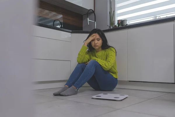 Önünde ağırlık tartısıyla flor 'da oturan perişan olmuş genç Asyalı kadın. Kilo kaybı ve akıl sağlığı konsepti — Stok fotoğraf