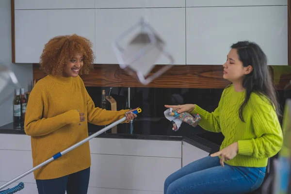 Duas jovens mulheres se divertindo enquanto fazem limpeza em casa. Amizade ou relacionamento multirracial — Fotografia de Stock