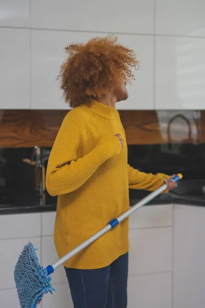 Jovem afro-americana negra feliz mulher usando esfregona como guitarra enquanto limpa a cozinha — Fotografia de Stock