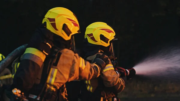 Los bomberos apagan el fuego con la manguera. Taladro de incendio de la casa en llamas —  Fotos de Stock