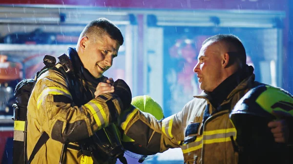 Retrato de dos jóvenes bomberos sobre la lluvia frente al camión de bomberos en uniforme completo. Deriva de fuego —  Fotos de Stock