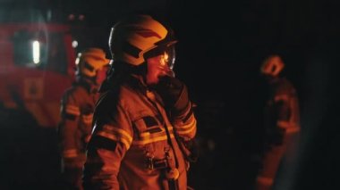 İtfaiyecilerin iş arkadaşlarıyla konuşmak için telsiz kullanmalarına yakın çekim. Arka planda acil durum ışıkları ve iki itfaiyeci daha var.