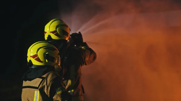 Пожежники гасять вогонь шлангом. Будівництво пожежного буріння. Вид ззаду — стокове фото
