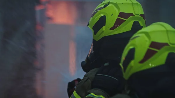 De perto, dois bombeiros extinguem o fogo, pulverizando com mangueira à noite. — Fotografia de Stock