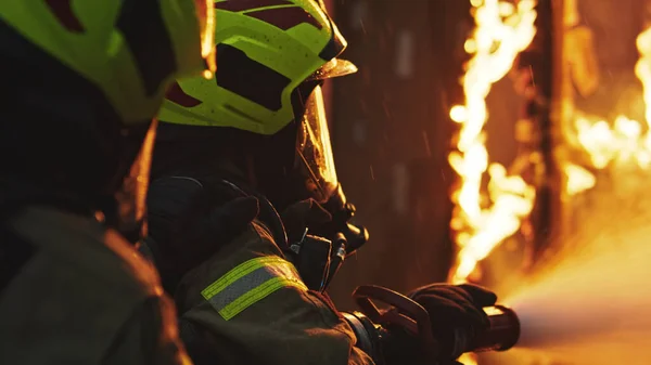 Los bomberos apagan el fuego con la manguera. Taladro de incendio de la casa en llamas —  Fotos de Stock