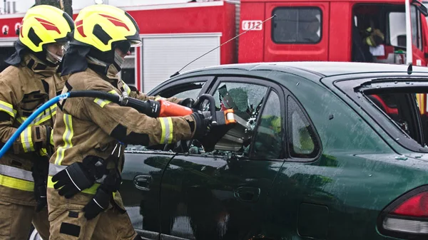 Tűzoltó beraking üveg segítségével jaws az élet, hogy kiszabadítsa csapdába esett áldozat az autóból — Stock Fotó