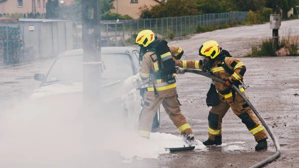 Bombeiros extinguem fogo do carro em chamas usando espuma — Fotografia de Stock