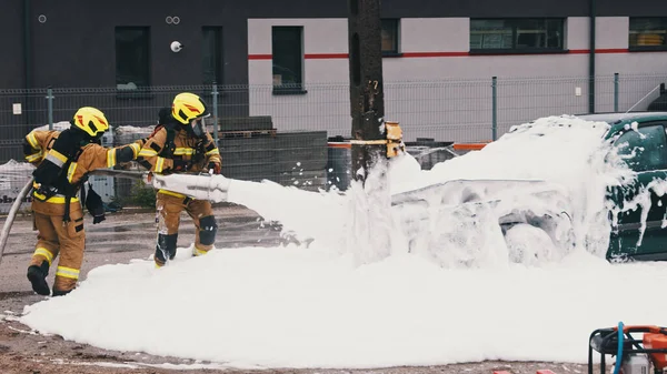 Bomberos extinguir el fuego del coche en llamas con espuma —  Fotos de Stock