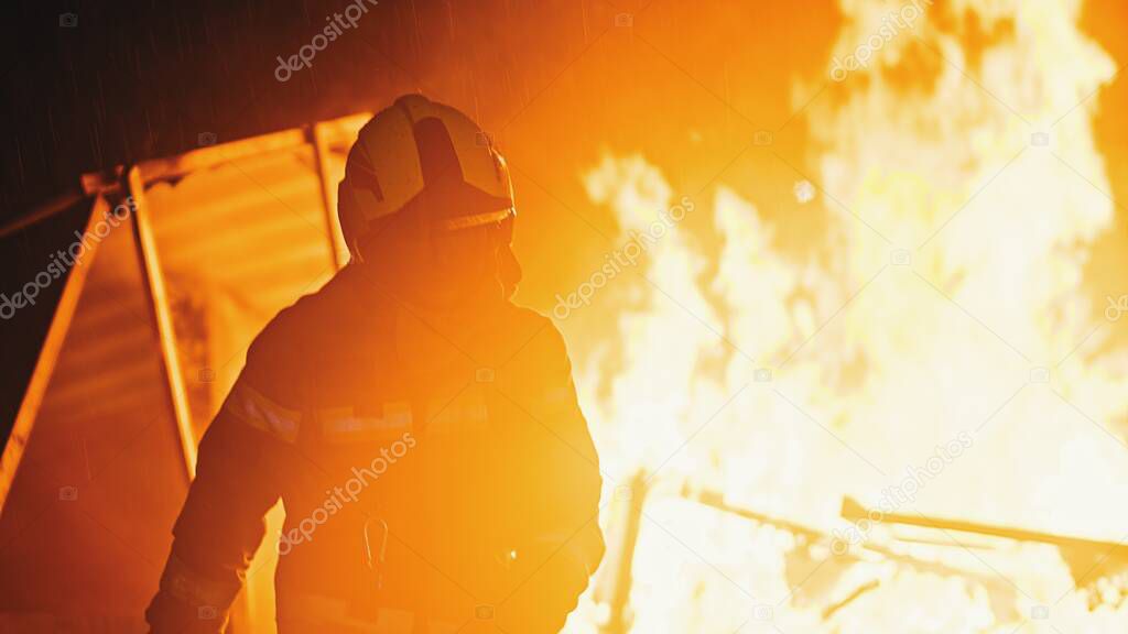 Unrecognizable fireman in front of the flames of burning house