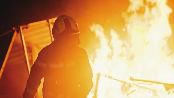 Bombero irreconocible frente a las llamas de la casa en llamas — Vídeo de stock