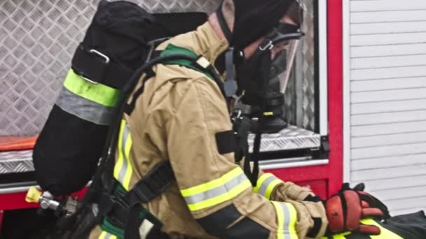Fireman with gas mask putting on safety hemet in front of the fire engine — Stock Video