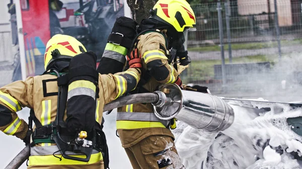 Taladro de fuego. Bomberos extinguir el fuego desde el coche de enfermería utilizando la espuma —  Fotos de Stock