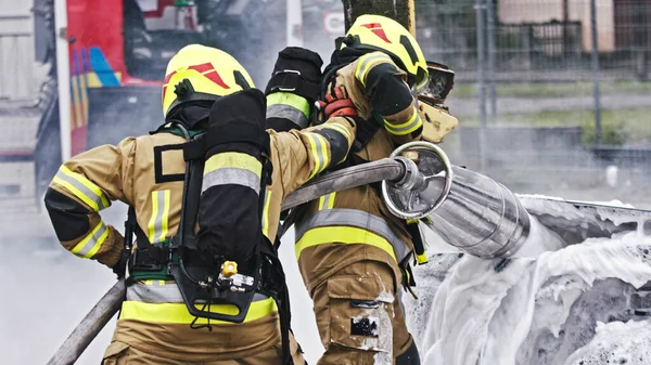 Taladro de fuego. Bomberos extinguir el fuego desde el coche de enfermería utilizando la espuma —  Fotos de Stock