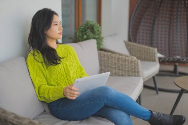 Genç Asyalı kadın balkonunda dizüstü bilgisayar kullanıyor. Ev eğlencesi ya da uzaktan öğrenme kavramı