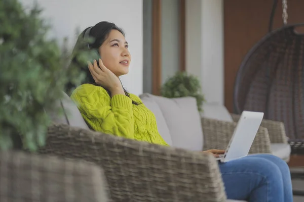 Joven mujer asiática, freelancer, trabajando en su portátil con auriculares. Aprendizaje a distancia o concepto de trabajo remoto — Foto de Stock