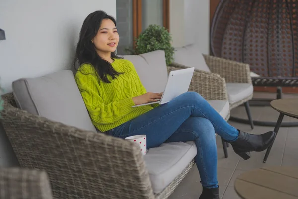 Jovem mulher asiática usando laptop em sua varanda. Conceito de entretenimento doméstico ou ensino à distância — Fotografia de Stock